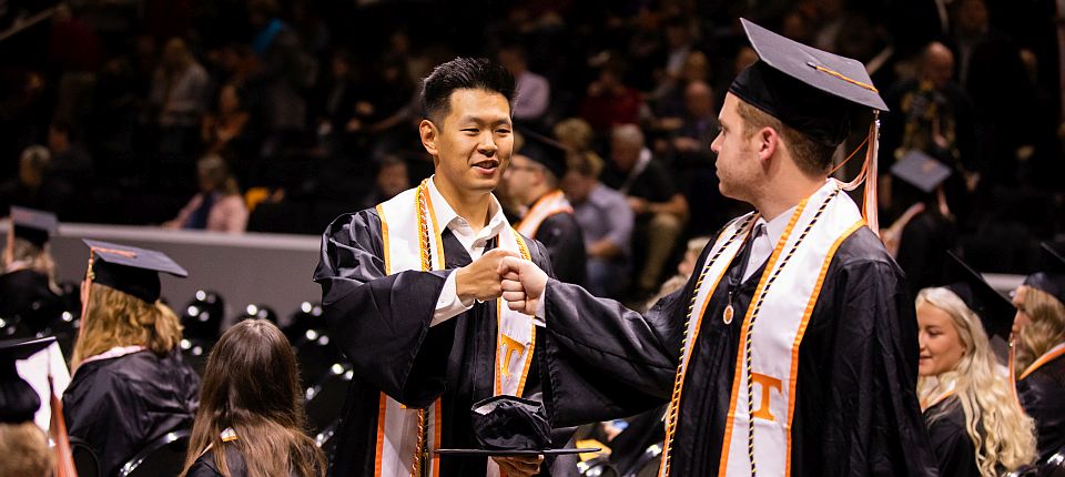 2 students at graduation fist bumping